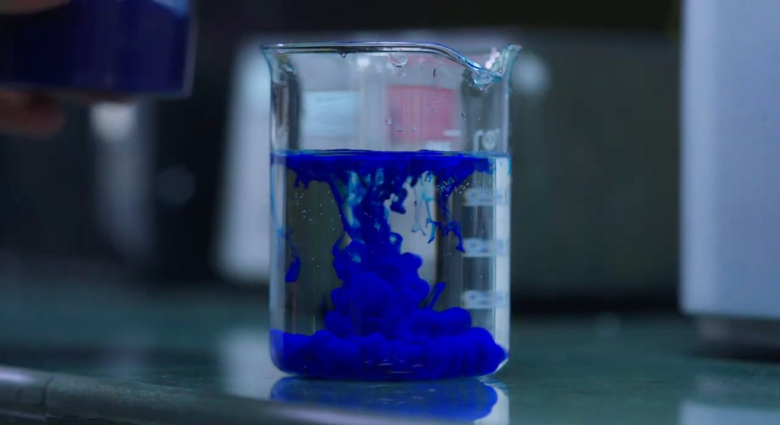 Blue dispersion swirling through water in a laboratory beaker
